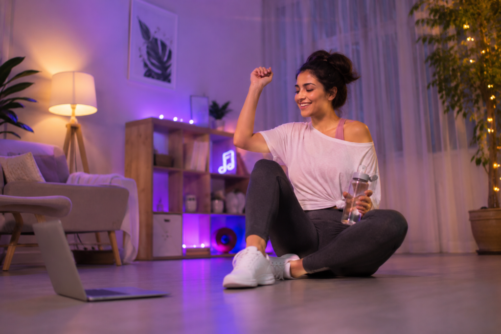 Dance fitness workout at home with a woman resting after exercise in a softly lit living room.